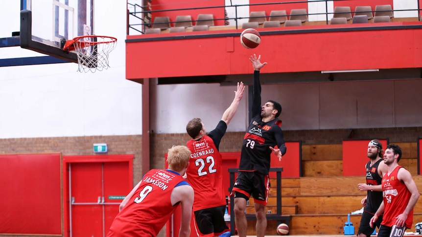 basketball player attempts a lay-up while opponent attempts to block and other players stand by