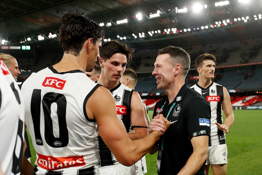 Craig McRae and Scott Pendlebury smile and shake hands after an AFL match.