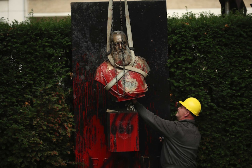 A bust of Belgium's King Leopold II, is hoisted off of its plinth by a crane as it's removed from a park in Ghent, Belgium.