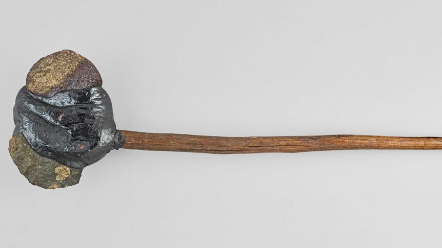 A rock attached to a slim wooden handle.