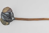 A rock attached to a slim wooden handle.