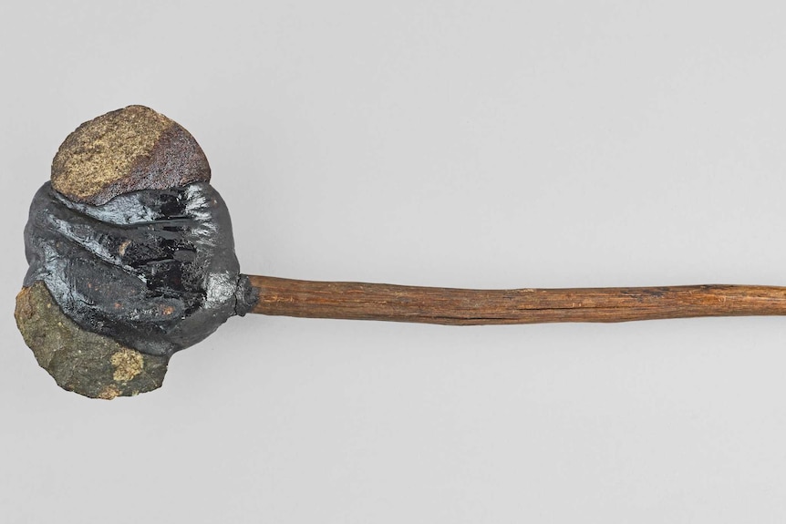 A rock attached to a slim wooden handle.