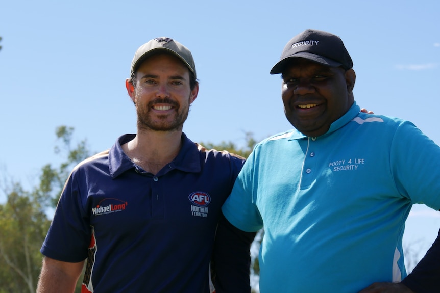 Two smiling men, both wearing caps and sports shirts.