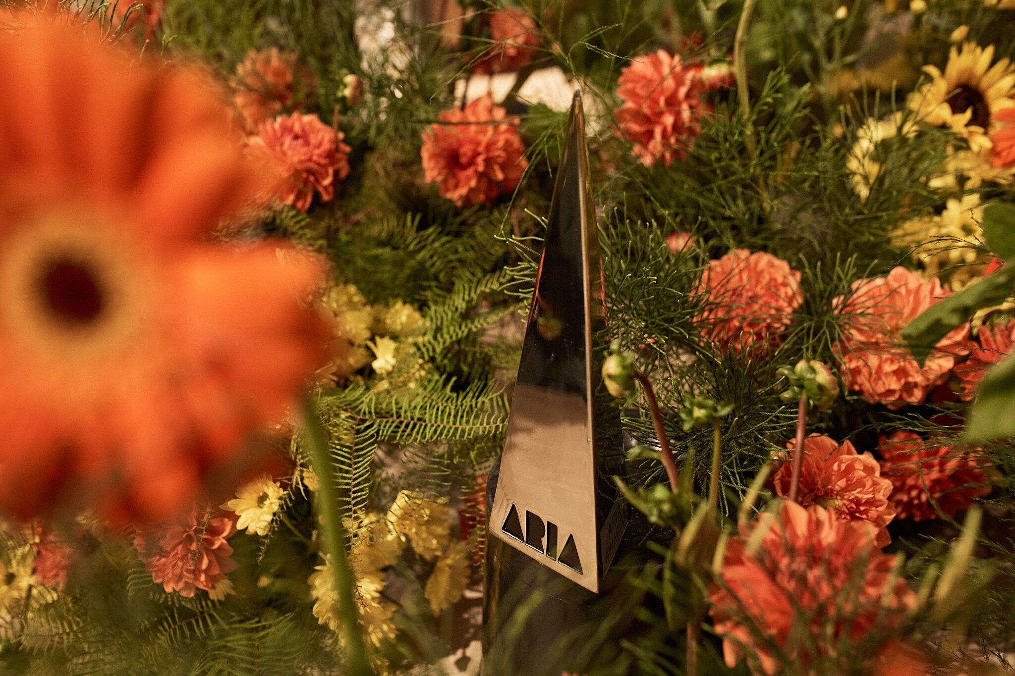 An ARIA award surrounded by orange flowers and greenery