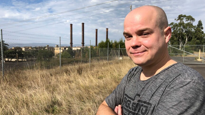 Jarrod Rich stands outside the fence of a coal-fired power station. There are smoke stacks in the distance.