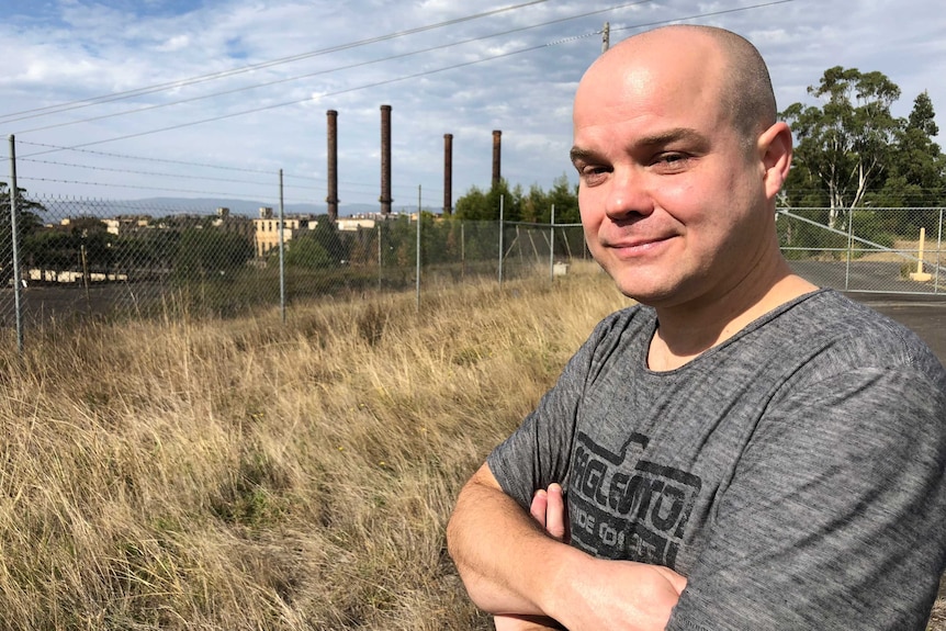 Jarrod Rich stands outside the fence of a coal-fired power station. There are smoke stacks in the distance.