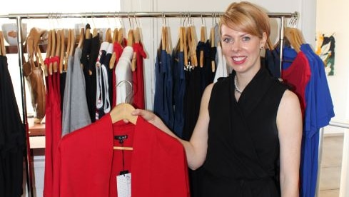 A dress designer holding up a red jacket.