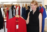 A dress designer holding up a red jacket.