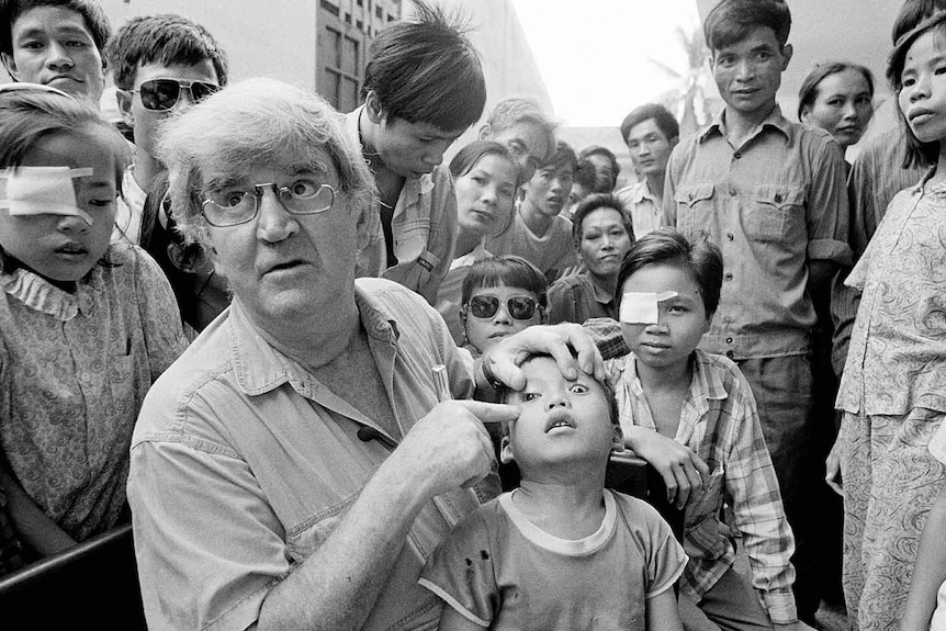 Dr Hollows points to a young boy's eye while a crowd of onlookers stare