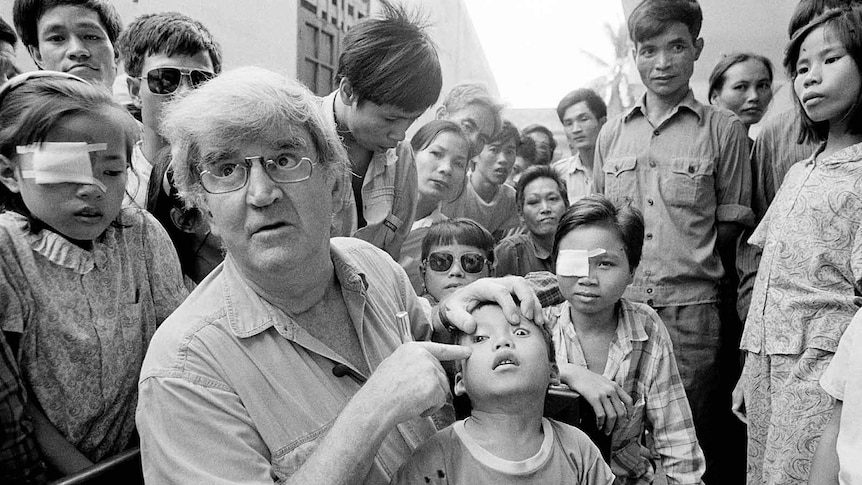 Dr Hollows points to a young boy's eye while a crowd of onlookers stare