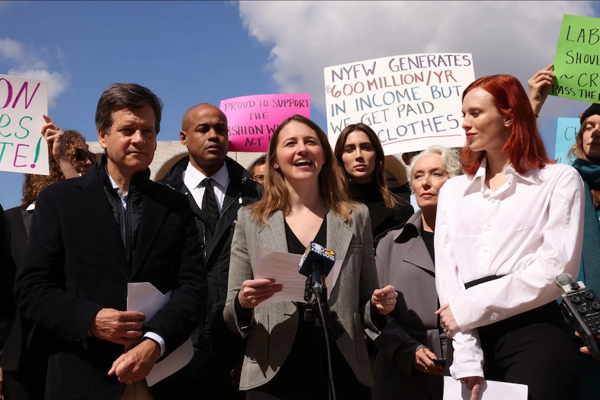 a group of people with placards surrounding a young woman with a microphone