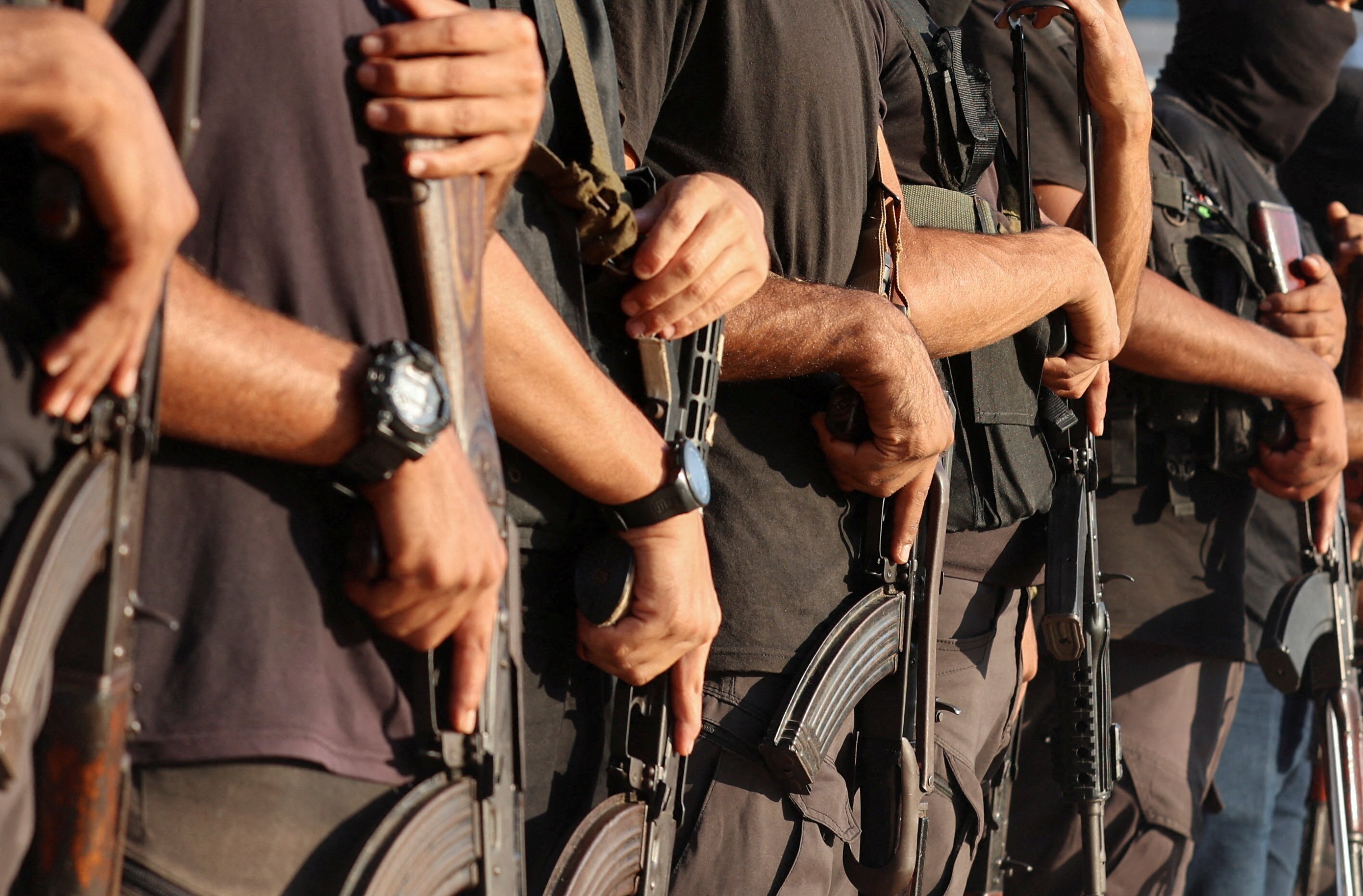 A close up image of a row of people in dark clothing holding guns (no faces showing).
