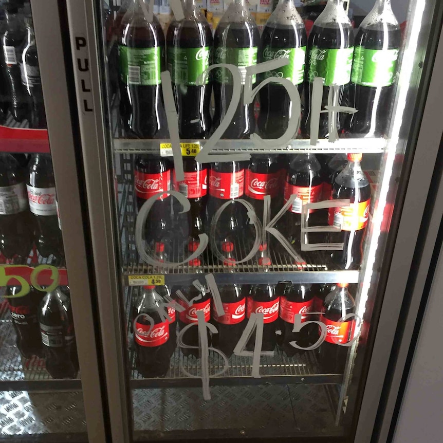 Fridge of drinks with handwritten sign saying $4.50 Coke cost