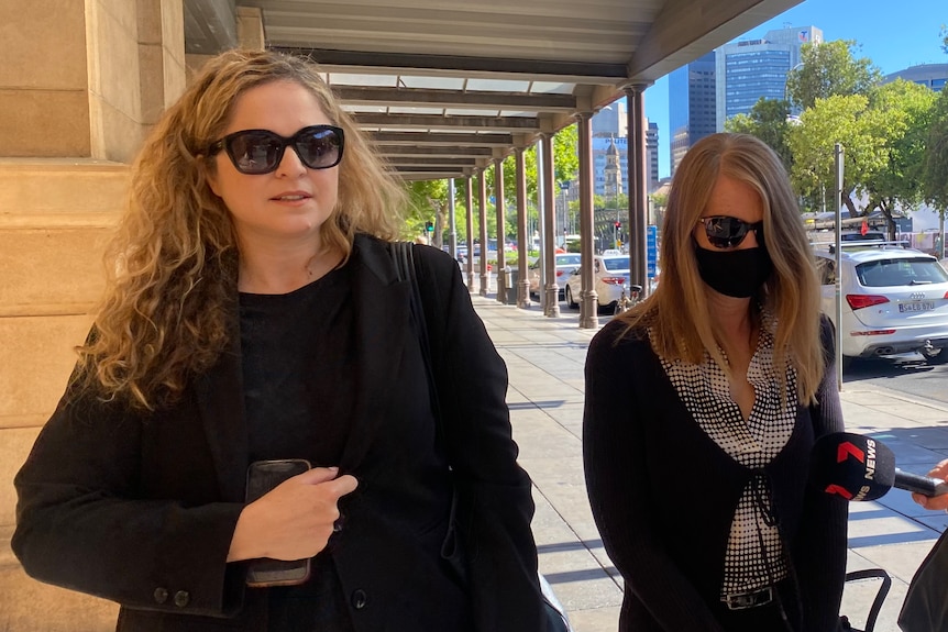 Two ladies in black wearing sunglasses walking outside court 