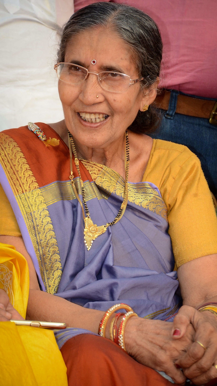 A close up of a woman wearing a bindi on her forhead and glasses as she smiles.