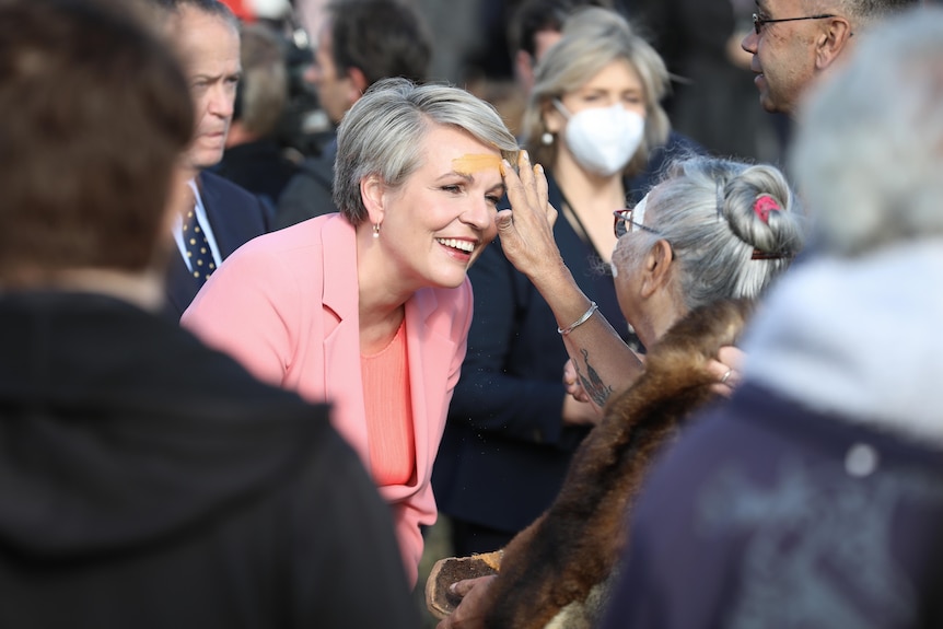 Plibersek smiles as an elder paints ochre on her forehead outside Parliament.