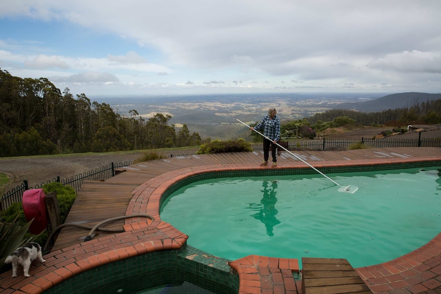 A woman skims a swimming pool in front of a sweeping vista of fields and hills.