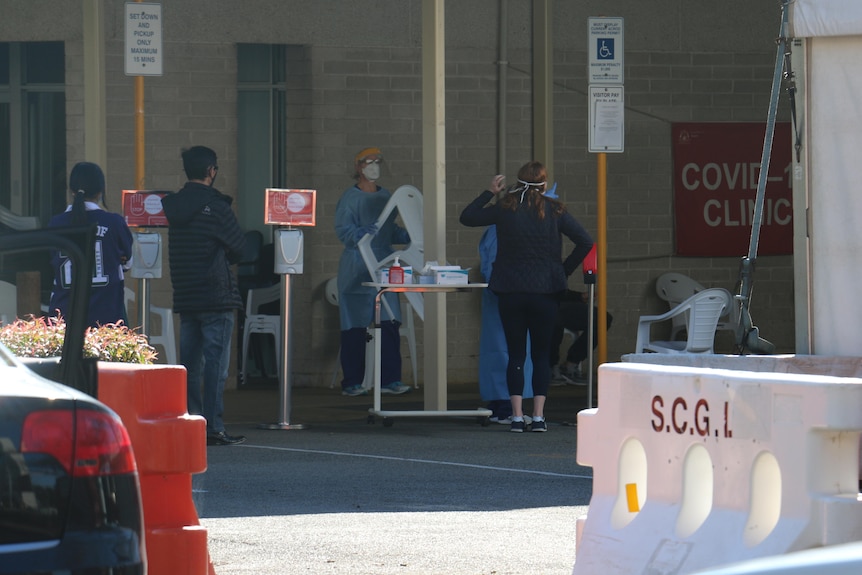 A COVID testing clinic with people queuing outside and staff wearing PPE.