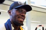 Usain Bolt smiles at the camera with a group of children looking on