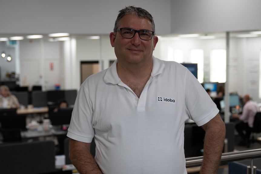 A man wearing a white polo shirt and glasses smiles at the camera.