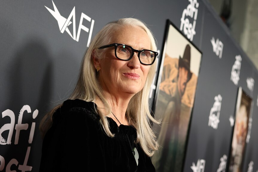 67-year-old white woman with long white hair wearing black-rimmed glasses and black top, seen from side on and below.