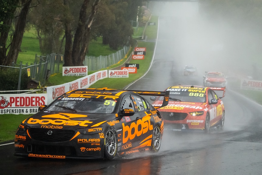 Birightly coloured race cars emerge from a grey mist on wet bend in the track 