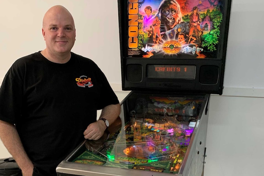 Man standing beside a pinball machine smiling