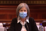 A woman with grey hair wearing a face mask and a black jacket in a room