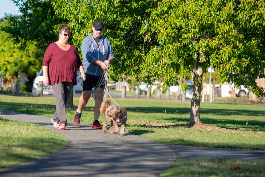 A man and woman walk a dog through a park.