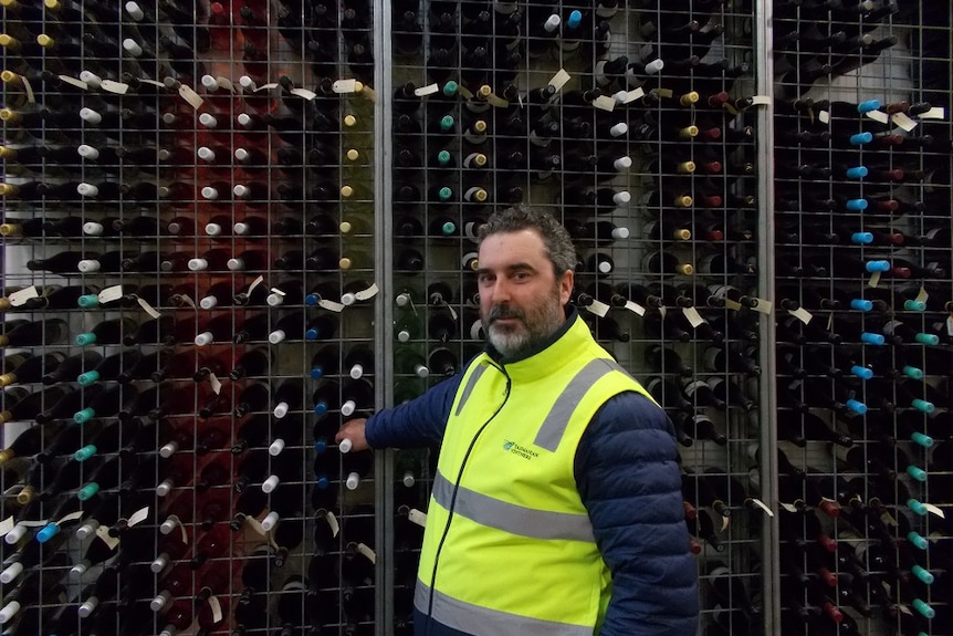 A man stands in front of a shelf of wine bottles.