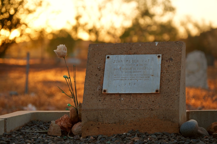 The gravesite of John Peter Pat at sunset. A single plastic flower is at the grave.