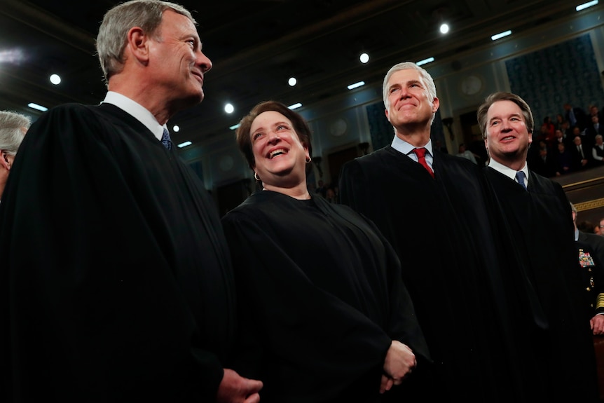 Four of nine US supreme court judges in black robes smile amongst themselves.