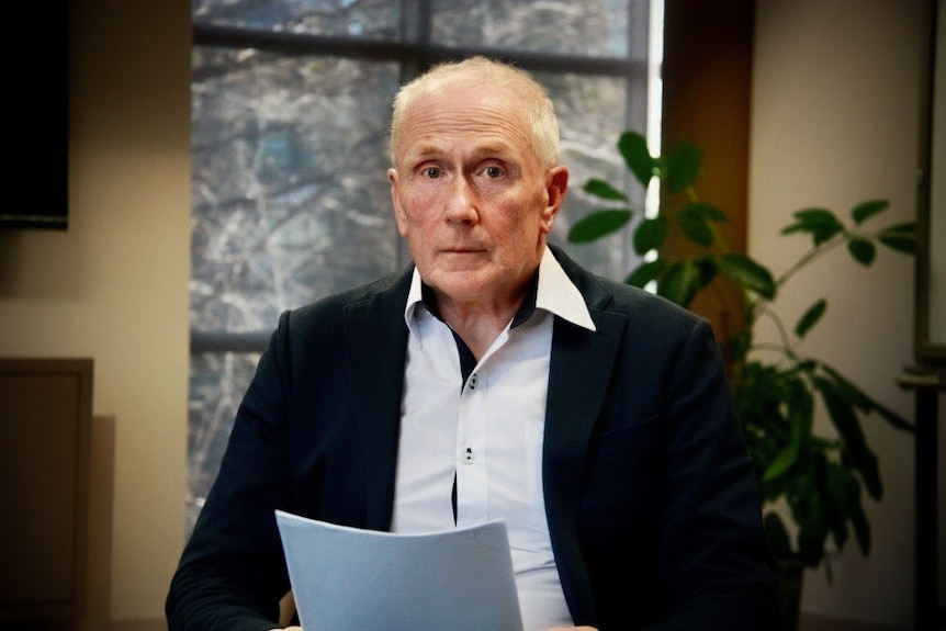 David Pumpton, holding documents, looks at the camera.