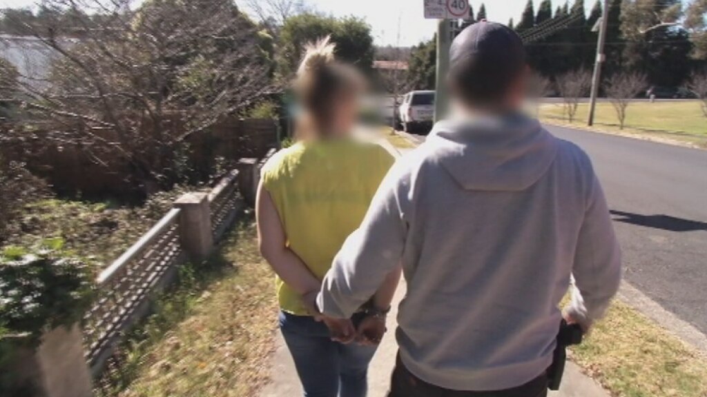 A handcuffed woman is led away from a property by a police officer
