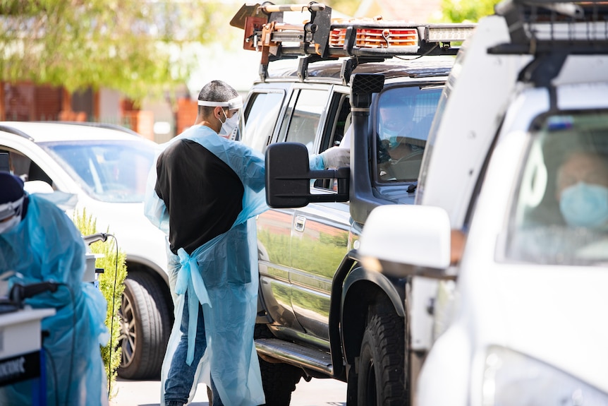 A man in PPE reaching into a car.