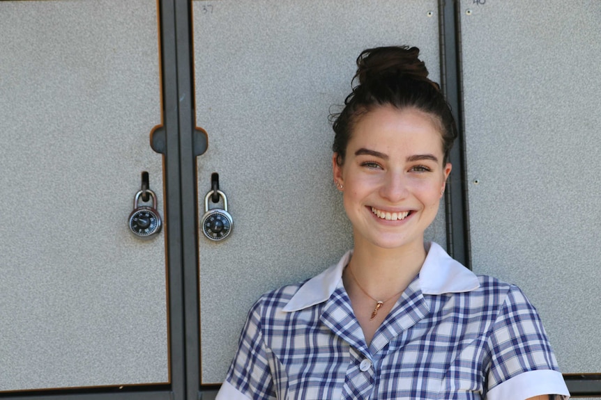 A young girl in a school uniform stands in front of some school lockers.