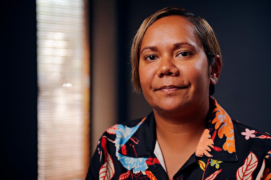 An Indigenous woman with short hair looks at the camera, sitting in her office.