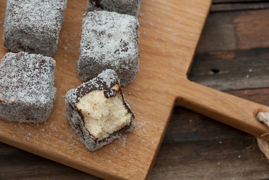 Four lamingtons, one of them half-eaten, sitting on a breadboard.