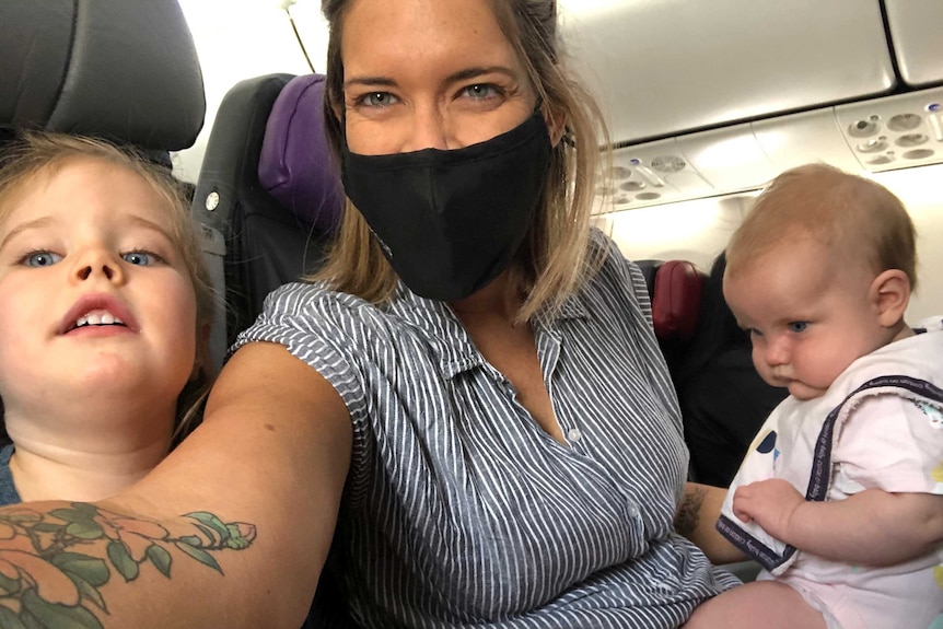 A woman wearing a mask with two young children on a plane.