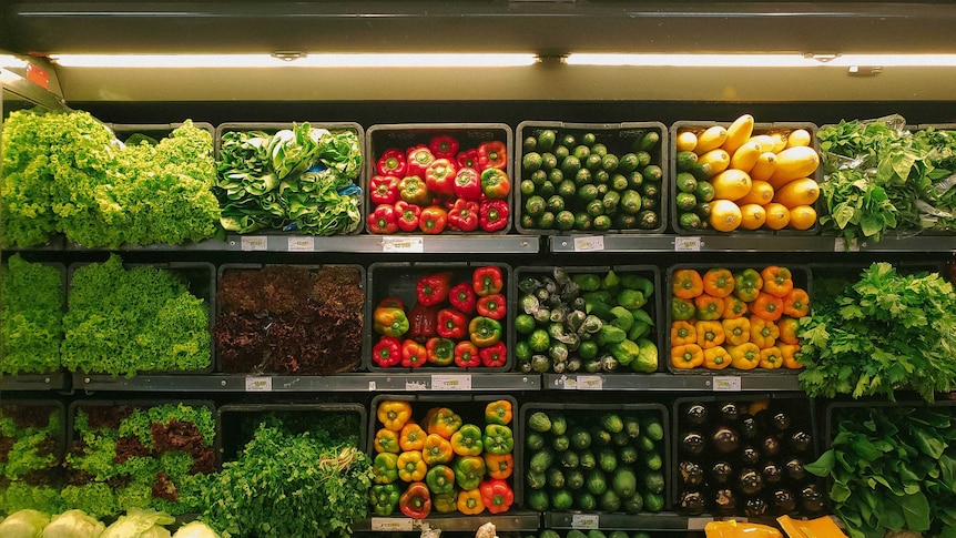Shelves of fresh produce at a grocery store - red capsicums, cauliflower, kale and cucumbers
