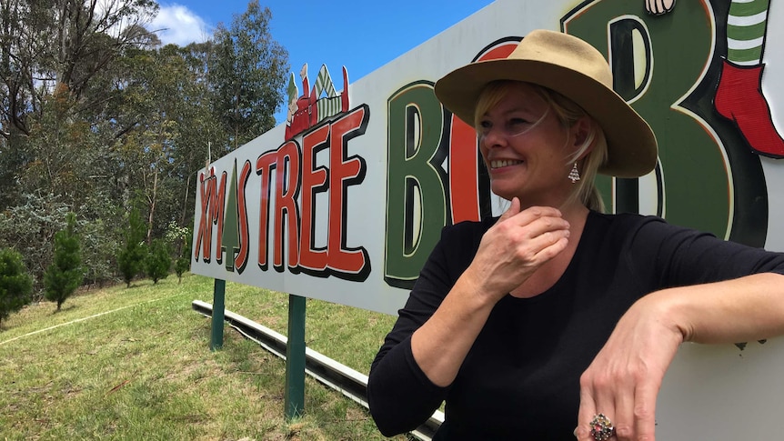 Deb Court leans against her business sign while laughing