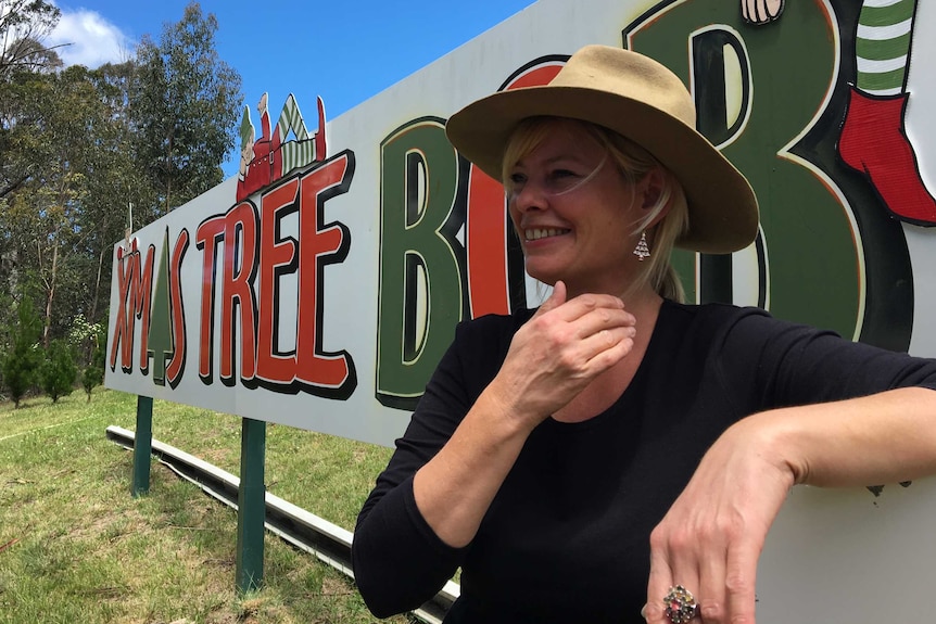 Deb Court leans against her business sign while laughing