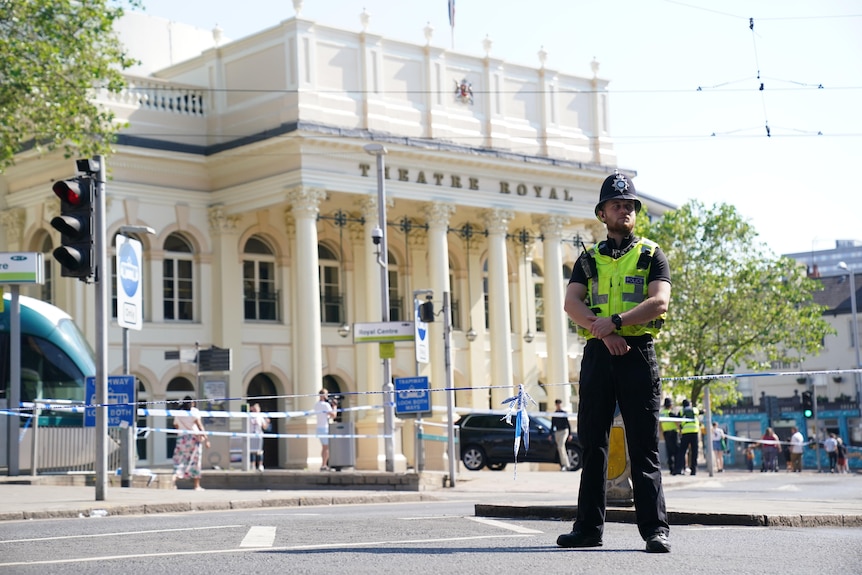 Nottinghamshire Police officer stands in front a a large building and closed road, arms crossed.