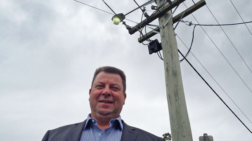 Energy consultant, Marc White standing in front of a power pole supporting overhead electricity wires