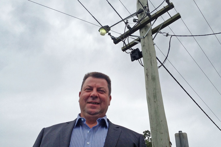 Energy consultant Marc White standing in front of a power pole supporting overhead electricity wires.