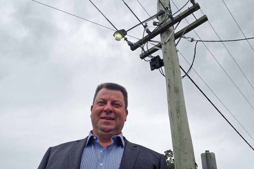 Energy consultant, Marc White standing in front of a power pole supporting overhead electricity wires