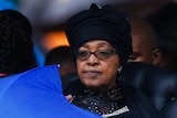 Winnie Madikizela-Mandela dressed in black and holding a blue umbrella at a memorial service for Nelson Mandela.
