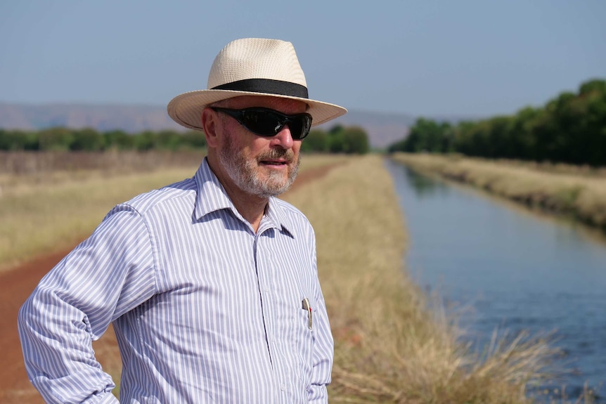 Close up of man standing in paddock with irrigation channel in the background