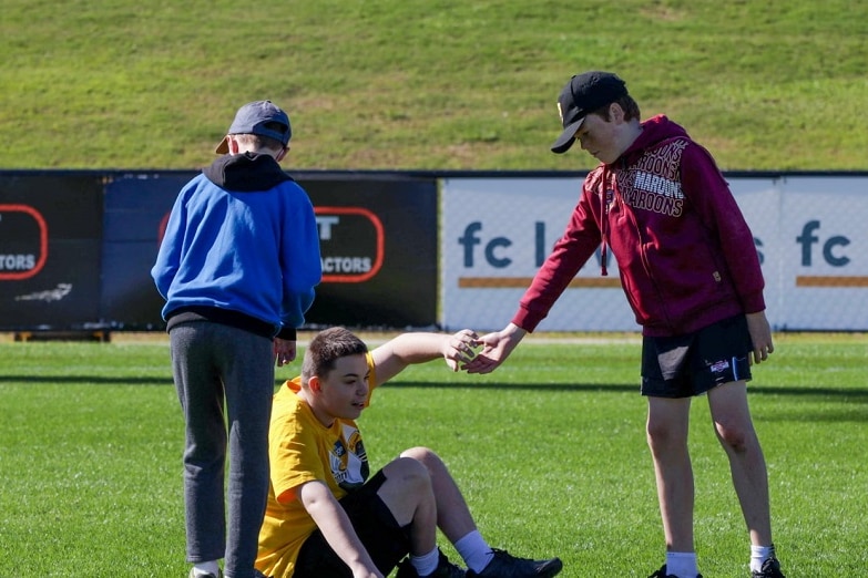 A young boy holding out his hand to another boy on the ground