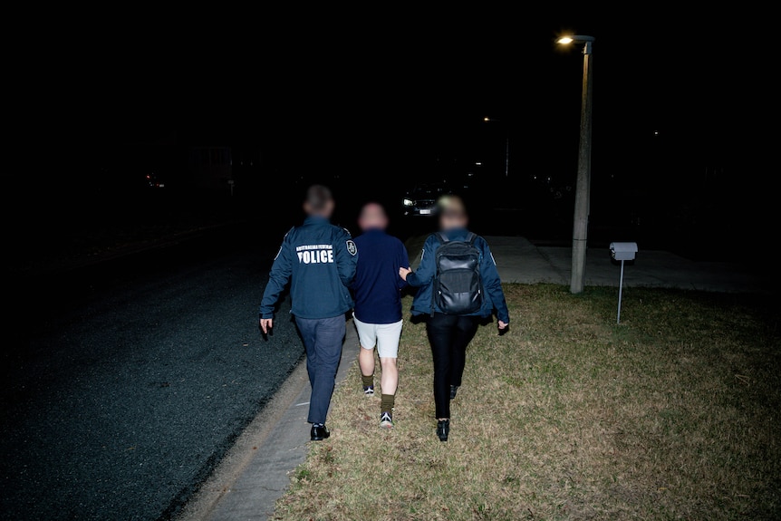 Two police officers lead away a man in handcuffs.